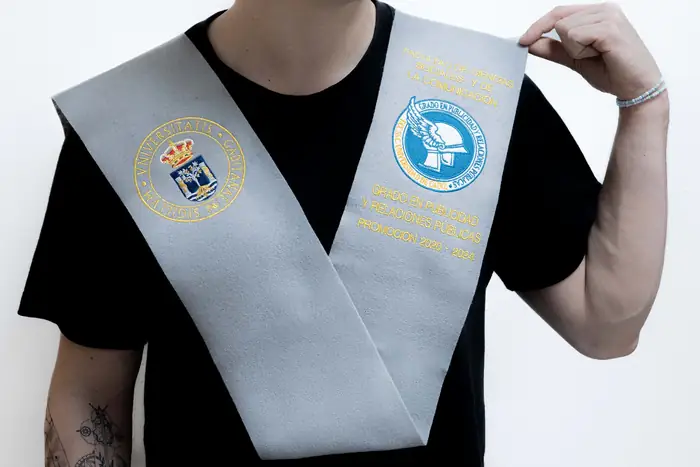 Beca gris claro con dos escudos bordados puesta sobre los hombros