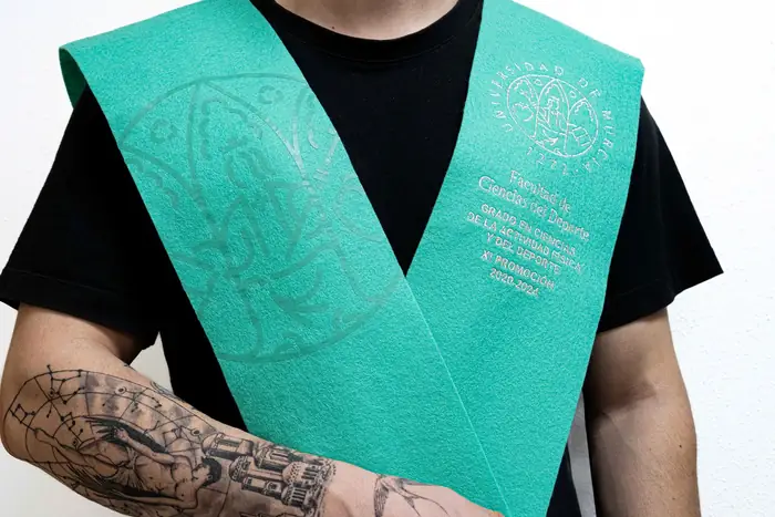 Beca verde con escudo bordado, sujeta por un graduado