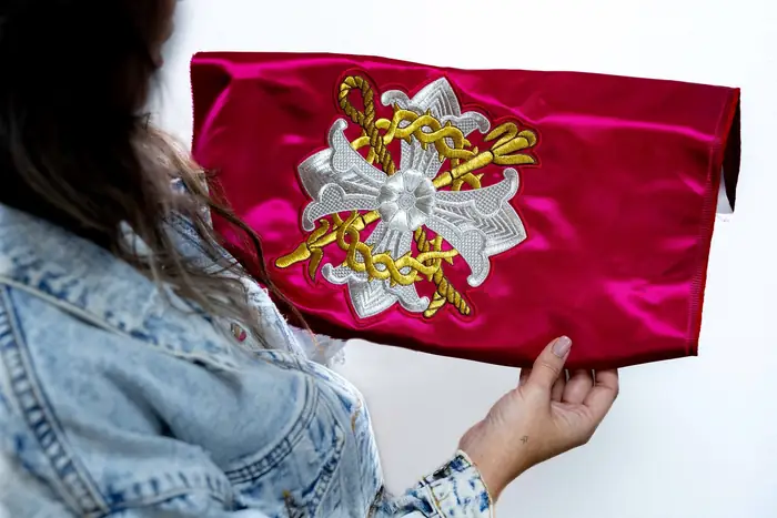 Manos sujetando un estandarte de terciopelo rojo bordado en plata y oro