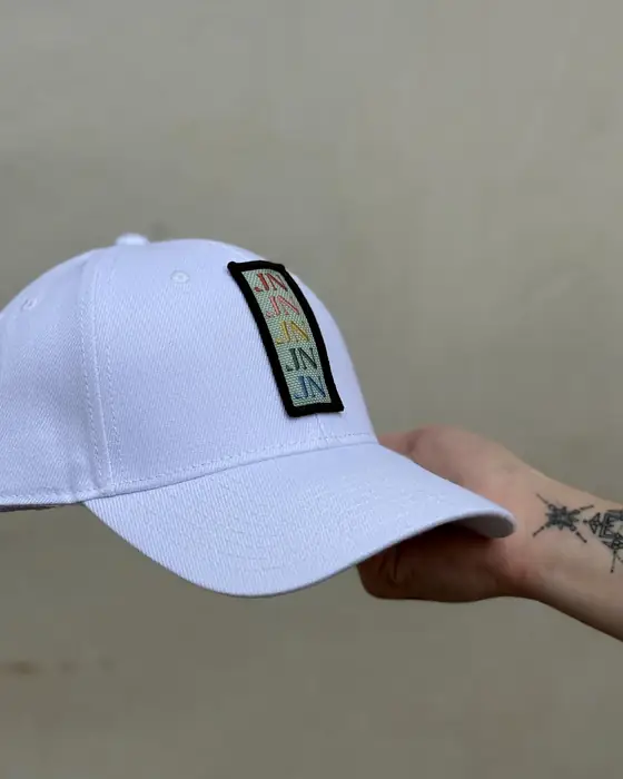 Gorra blanca con etiqueta tejida, sujeta en la mano