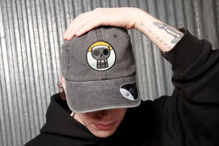 Gorra gris con calavera bordada, sujeta sobre la cara