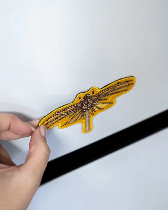 Mano sujetando un parche imantado con alas bordadas en oro