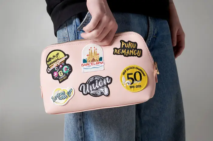 Neceser rosa con parches bordados aplicados, sujeto en la mano